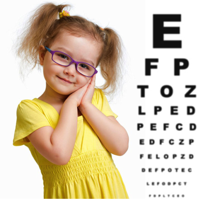 Smiling young girl with glasses posing cheerfully in front of an eye chart.