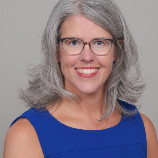 Smiling middle-aged woman with gray hair and glasses in a blue sleeveless top.